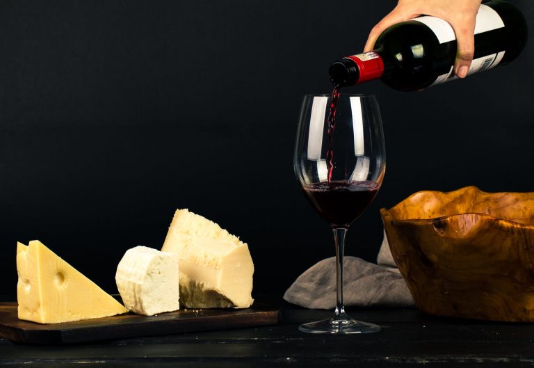photo of person pouring wine into glass besides some cheese pairings