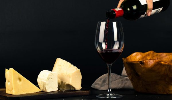 photo of person pouring wine into glass besides some cheese pairings